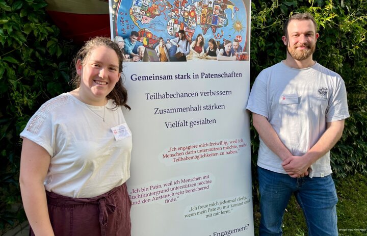 Zwei Menschen lächeln in die Kamera. Zwischen ihnen steht ein Transparent. - Link: Das Innovations-Sofa. Diesmal mit dem Team von Menschen stärken Menschen der Caritas in Zwickau