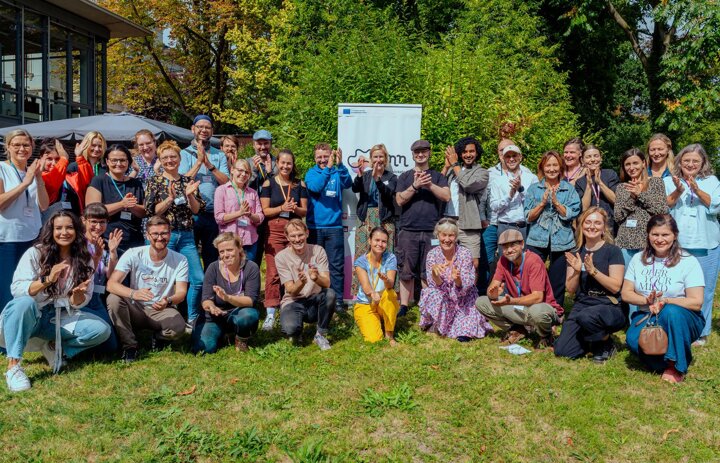Eine große Gruppe an Menschen steht und kniet auf einer Wiese. Die Menschen lächeln in die Kamera. - Link: Viele neue Gesichter - der SINNkubator geht in Runde 4