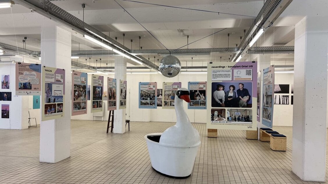 Man sieht einen großen, offen Raum. in diesem hängen Plakate. Außerdem ist eine große Schwanstatue zu sehen. - Ausstellung zu sozialen Innovationen jetzt in Dresden