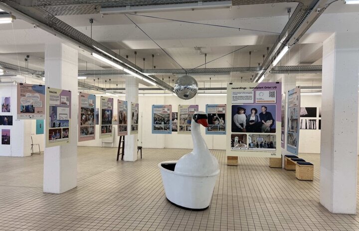 Man sieht einen großen, offen Raum. in diesem hängen Plakate. Außerdem ist eine große Schwanstatue zu sehen. - Link: Ausstellung zu sozialen Innovationen jetzt in Dresden