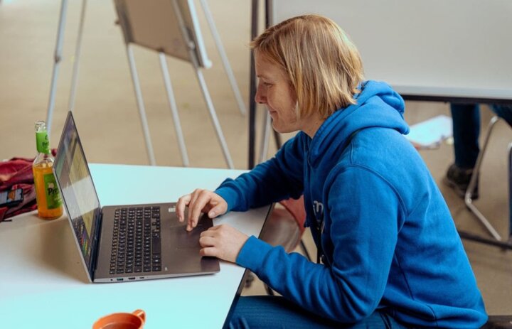 Eine Frau sitzt an einem Laptop. Sie ist von der Seite zu sehen. - Link: SINN Online-Werkstatt - digitales Treffen für eure Anliegen