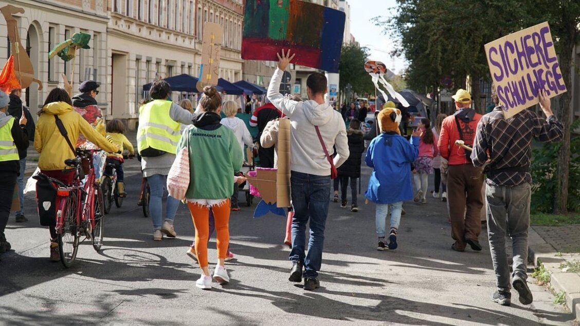 Menschen gehen bei einer Demonstration eine Straße entlang. Sie sind von hinten zu sehen. - Das Innovations-Sofa. Diesmal mit Superblocks Leipzig e.V.