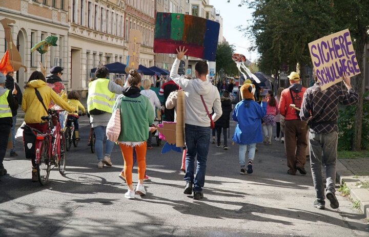 Menschen gehen bei einer Demonstration eine Straße entlang. Sie sind von hinten zu sehen. - Link: Das Innovations-Sofa. Diesmal mit Superblocks Leipzig e.V.