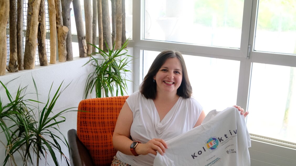 Eine Frau sitzt auf einem Sessel. Sie hält ein Shirt in der Hand auf dem Kollektiv steht. - Das Innovations-Sofa. Diesmal mit KolLEktiv - Treffpunkt für Engagement und Begegnung