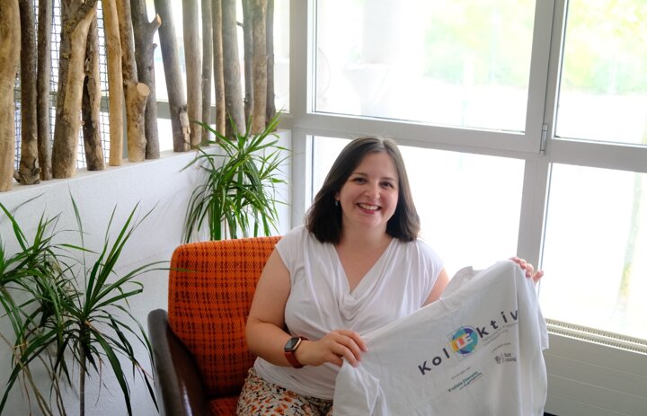 Eine Frau sitzt auf einem Sessel. Sie hält ein Shirt in der Hand auf dem Kollektiv steht. - Link: Das Innovations-Sofa. Diesmal mit KolLEktiv - Treffpunkt für Engagement und Begegnung