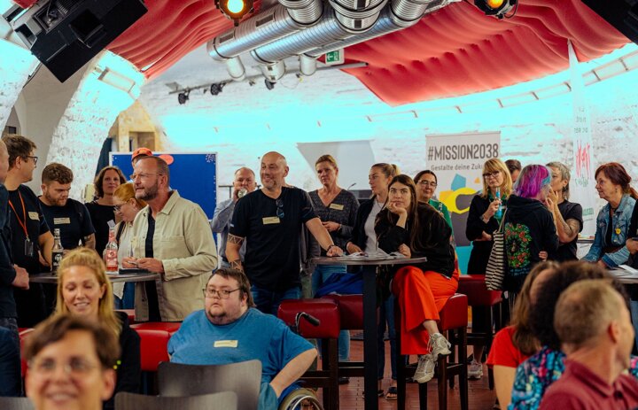 Viele Menschen sitzen und stehen in einem Raum. Manche unterhalten sich. - Link: Acht Stationen voller Vernetzung - Roadshow Torgau am 09.09.