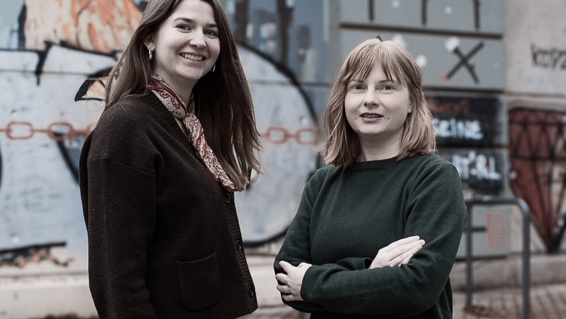 Zwei Frauen stehen nebeneinander und lächeln in die Kamera. Im Hintergrund ist eine Häuserwand zu sehen. - Das Innovations-Sofa. Diesmal mit dem MedienDemokratieHub