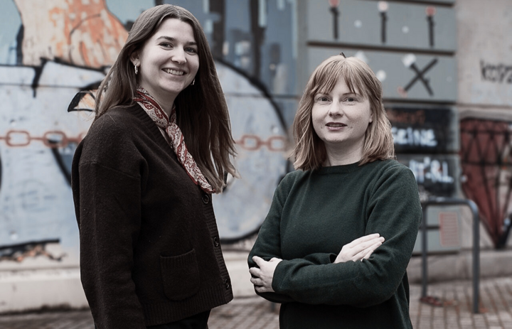 Zwei Frauen stehen nebeneinander und lächeln in die Kamera. Im Hintergrund ist eine Häuserwand zu sehen. - Link: Das Innovations-Sofa. Diesmal mit dem MedienDemokratieHub